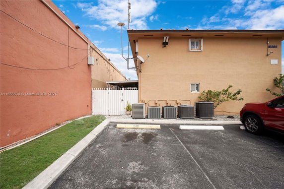 Outdoor parking area beside a building with air conditioning units and a vehicle.