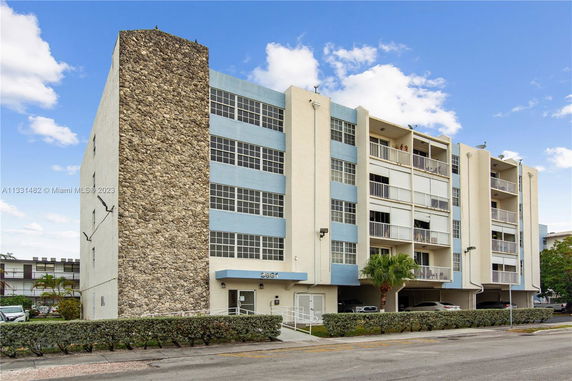 Front view of a multi-story building with a stone accent wall and blue and beige facade.