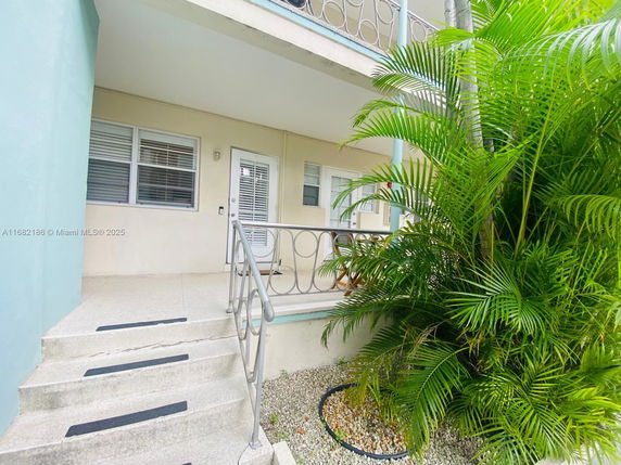 Front view of a building entrance with steps and railing, adjacent to a large plant.