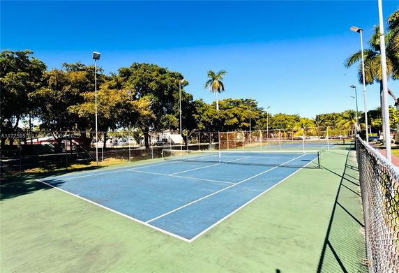 An outdoor tennis court surrounded by a fence, with trees in the background.