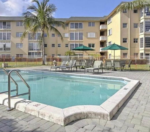 Outdoor swimming pool with sun loungers and umbrellas near a multi-story building.