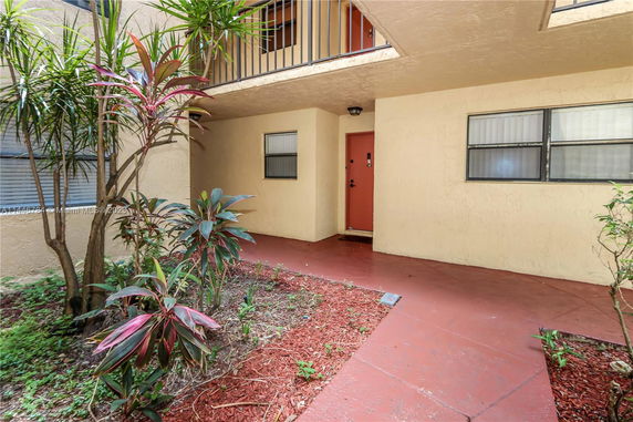 Entrance view of a residential building with beige walls and a red door.