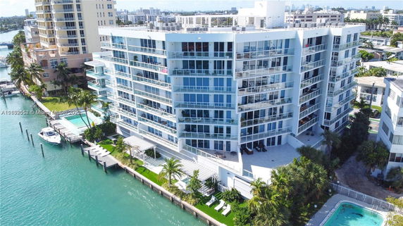 Aerial view of a modern multi-story residential building with glass balconies, located by the waterfront.