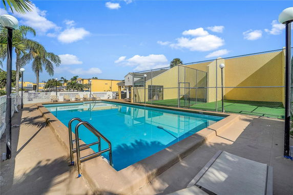 Outdoor swimming pool with surrounding fencing and lounge chairs.