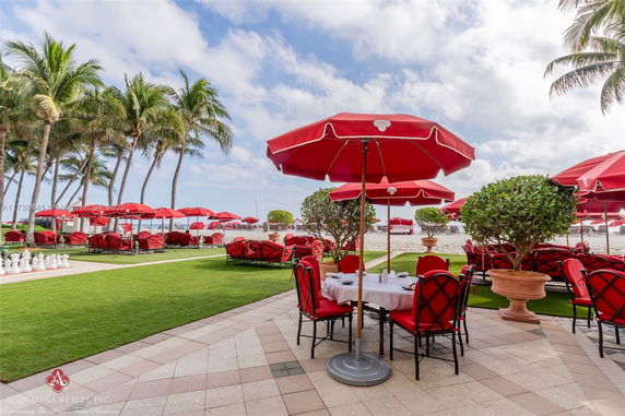 Outdoor seating area with red umbrellas and chairs near a beachfront.