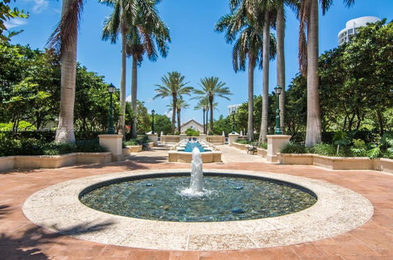 Fountain area with palm trees and benches.