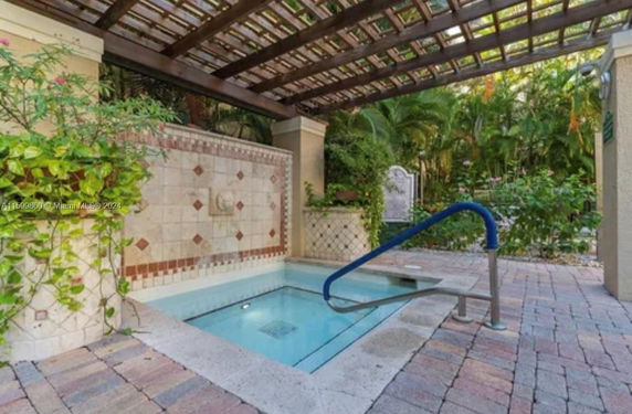 Small outdoor pool with decorative tiled wall and pergola.