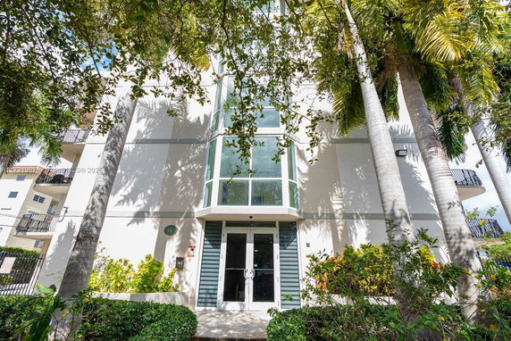 Front view of a multi-story building with large windows and surrounded by tall trees.