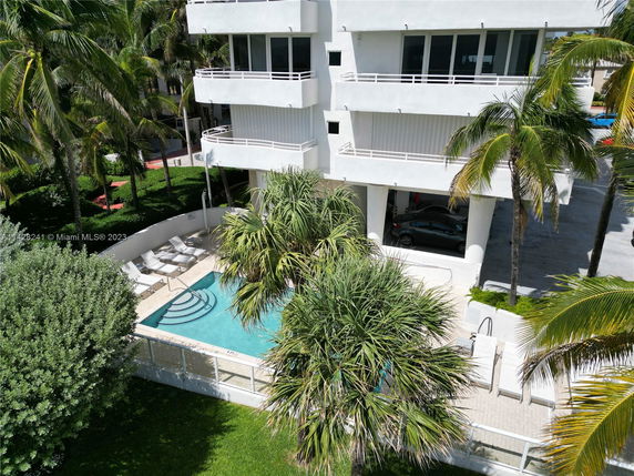 Aerial view of a swimming pool adjacent to a multi-story building with surrounding palm trees.