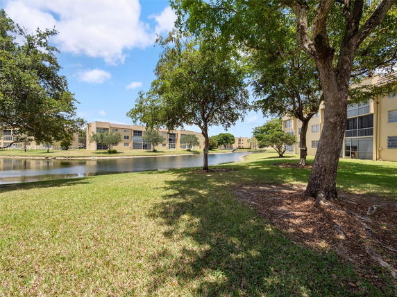 View of apartment buildings alongside a water body with trees and grass.