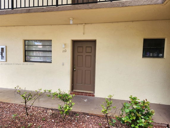 Front view of a ground-floor apartment entrance with a brown door and two windows.