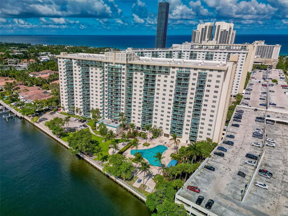 Elevated view of a beachfront high-rise building complex with balconies, pool area, and adjacent parking.