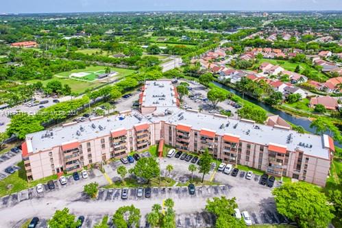 Aerial view of a multi-story apartment complex with parking areas and surrounding greenery.