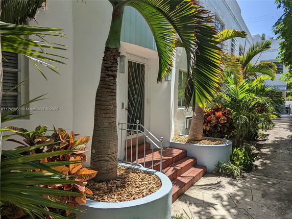 Front view of a building with plants and stairs leading to the entrance.