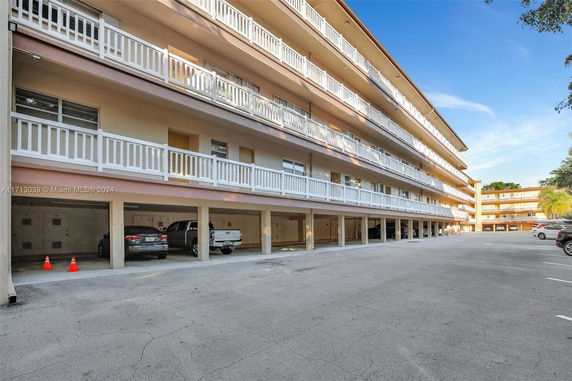 View of a multi-level apartment building with covered parking spaces underneath.