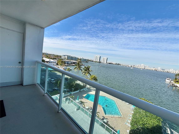 View from a balcony overlooking a waterfront with distant high-rise buildings and a swimming pool below.