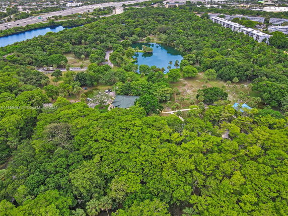 Aerial view of a lush green park with walking paths, ponds, and surrounding urban areas.
