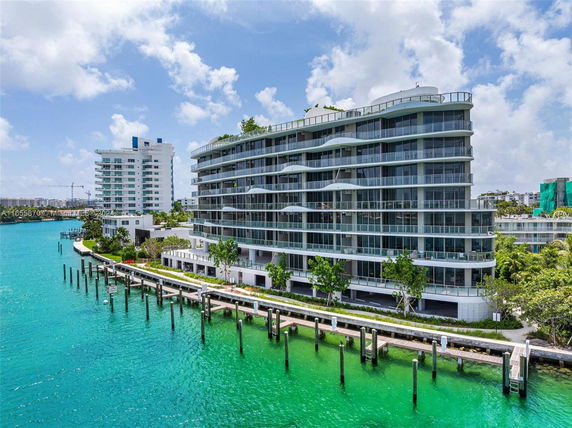 Waterfront view of a modern multi-story residential building with glass balconies.