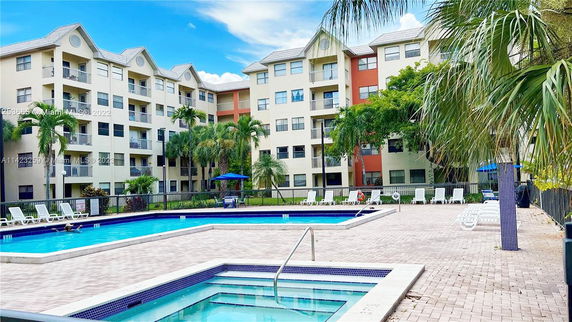 Outdoor swimming pool area in front of a multi-story apartment building.