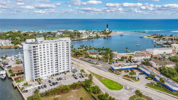 Aerial view of a coastal area with a tall residential building, roadways, and surrounding water bodies.