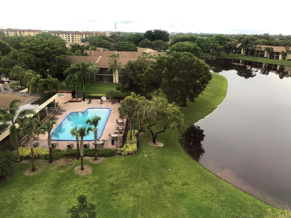 Panoramic view of a swimming pool and surrounding greenery with a lake visible.