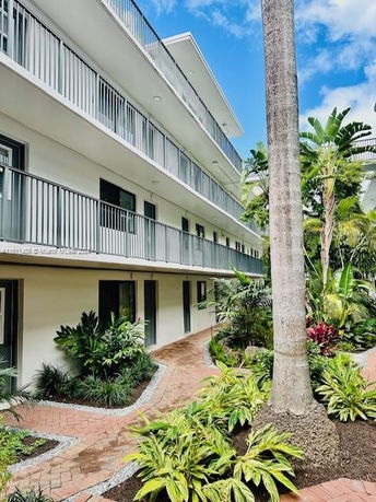 Exterior view of a multi-story building with balconies, surrounded by greenery and walkways.