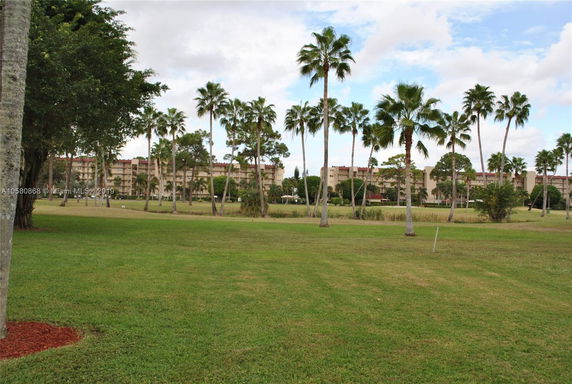 View of a multi-story building surrounded by palm trees and a grassy field.