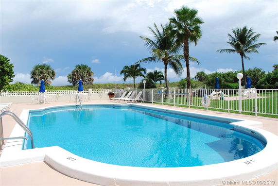 View of a swimming pool surrounded by palm trees and a fence.
