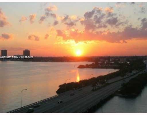 Panoramic view of a sunset over a body of water with a bridge and buildings in the distance.
