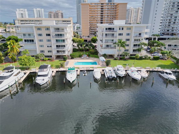 Aerial view of waterfront apartments with a swimming pool and docked boats.