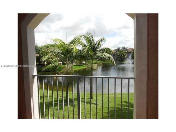 View from a balcony overlooking a scenic lake with palm trees and a fountain.