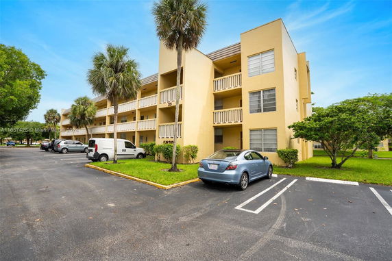Front view of a multi-story apartment building with balconies and parking area.