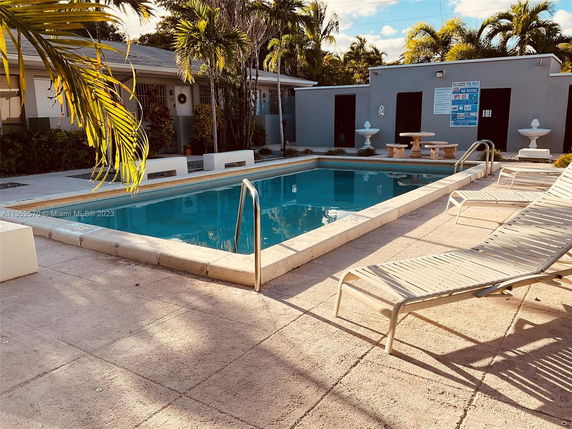 Outdoor swimming pool area with surrounding lounge chairs and tropical plants.