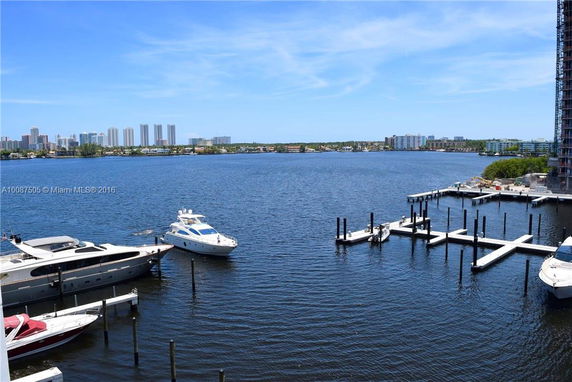 View of a marina with boats docked, overlooking a body of water and city skyline in the background.