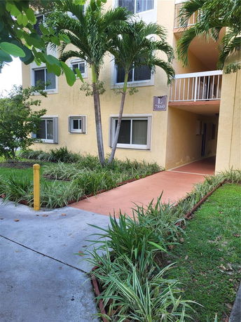 Front view of a yellow three-story building with a pathway and palm trees.