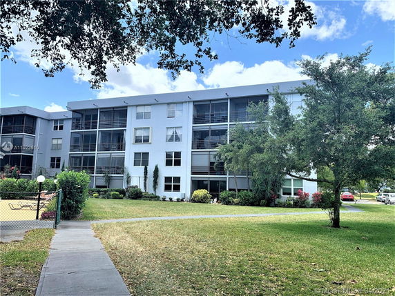 Front view of a multi-story residential building with balconies and surrounding greenery.