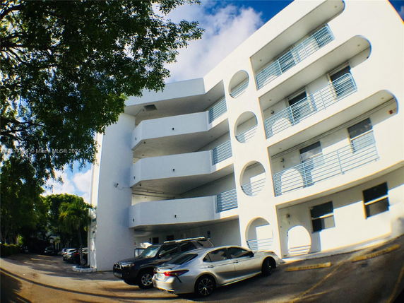 Front view of a multi-story building with balconies and a parking area.