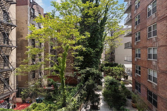 View between apartment buildings with visible fire escapes and greenery.