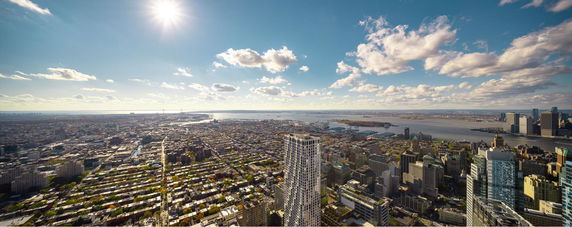 Wide-angle view of a cityscape with tall buildings, a river, and distant land under a sunny sky.