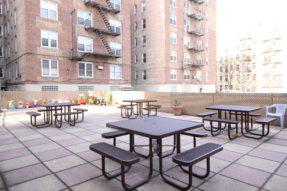 Outdoor area with picnic tables and children's play equipment, surrounded by residential buildings.