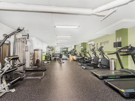 Interior view of a gym with various exercise equipment including treadmills, ellipticals, and weight machines.