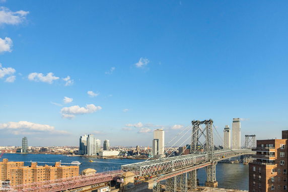 View of a bridge crossing over a river with city buildings in the background.