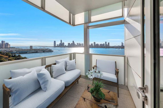 Balcony with comfortable seating overlooking a city skyline and water view.