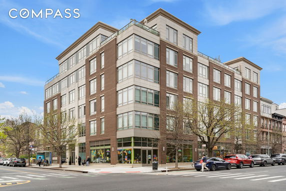 Street view of a multi-story apartment building with large windows and a brick facade.
