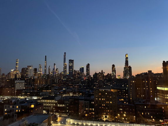 Panoramic view of a city skyline at dusk with illuminated skyscrapers against a darkening sky.