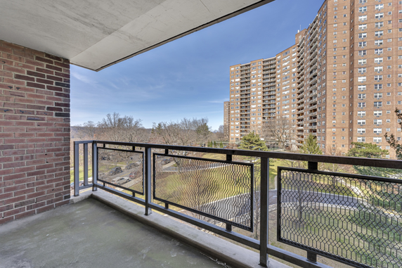 View from a balcony showing tall residential buildings and a green area below.