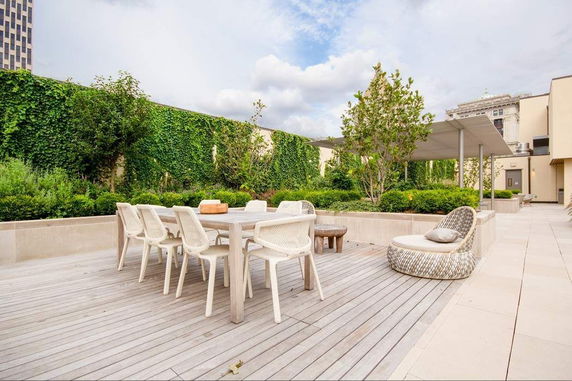 Rooftop area with dining table, chairs, and greenery.