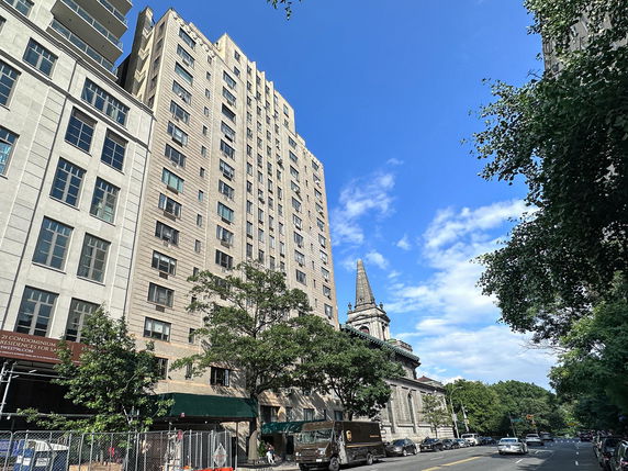 View of a tall residential building with multiple windows next to a historical building with a spire.