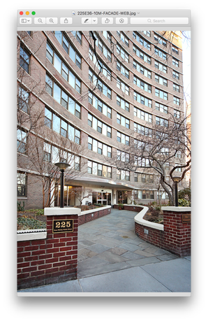 Front view of a multi-story apartment building with a curved facade and entrance pathway.