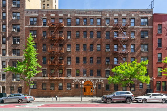 Front view of a multi-story brick apartment building with fire escapes.